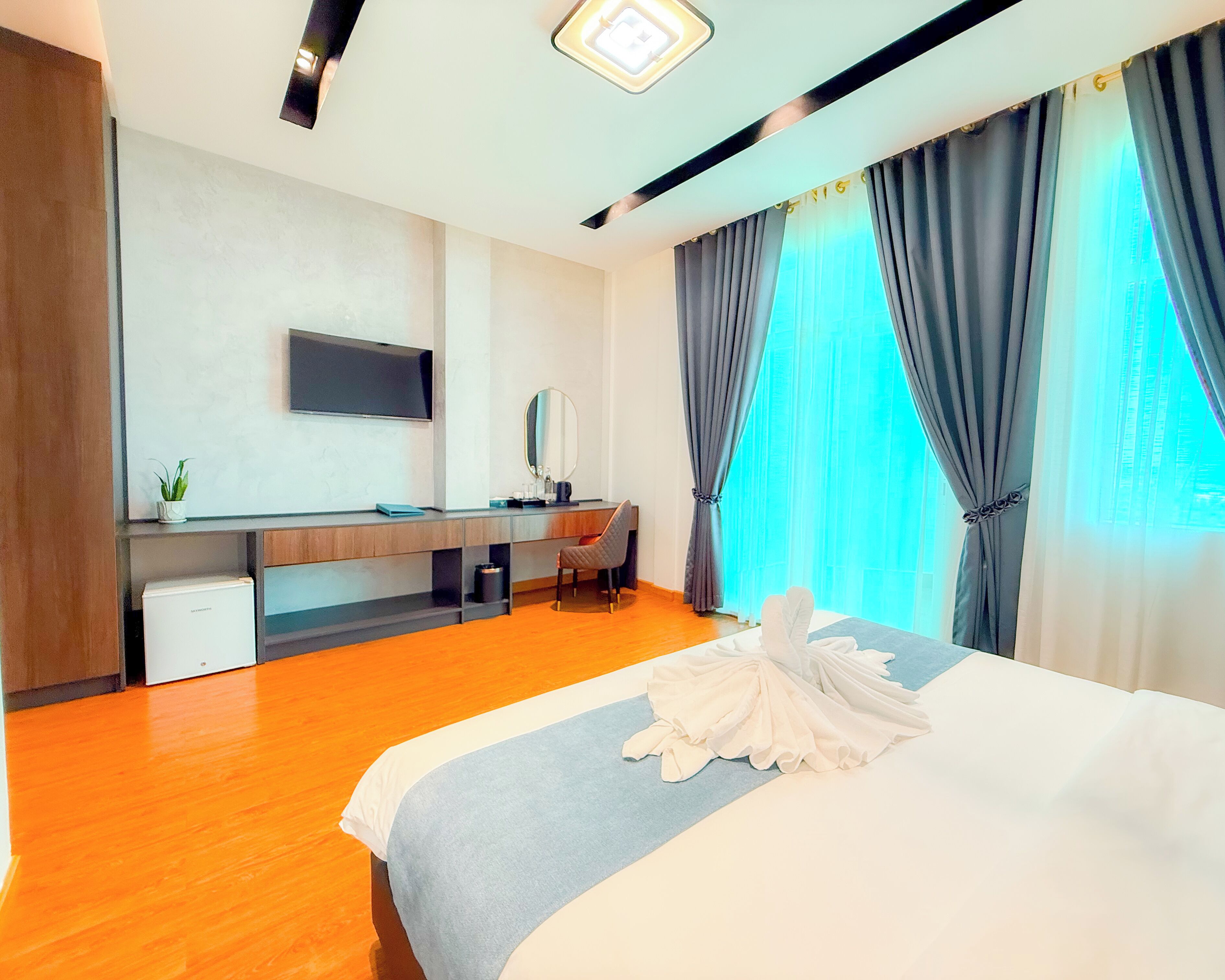 Une chambre d’hôtel avec un lit, un bureau, une chaise, une télévision et une fenêtre avec des rideaux.