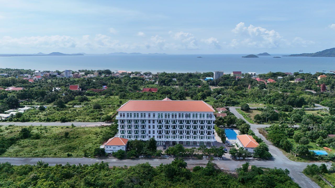Un hotel grande con varios pisos, rodeado de vegetación y vistas al mar.