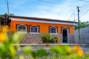 A two-story building with a red-tiled roof, orange walls, and a brick base. There are three windows on the second floor and a door on the ground floor. - Top Rated Home in Quezaltepeque, only 15 min away from San Salvador 🌅 (Quezaltepeque)