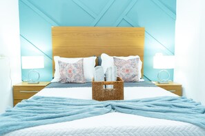 A neatly made bed with a blue blanket, a wooden headboard, and patterned pillows. There is a wicker basket on the bed and two bedside tables with lamps. - Top Rated Home in Quezaltepeque, only 15 min away from San Salvador 🌅 (Quezaltepeque)