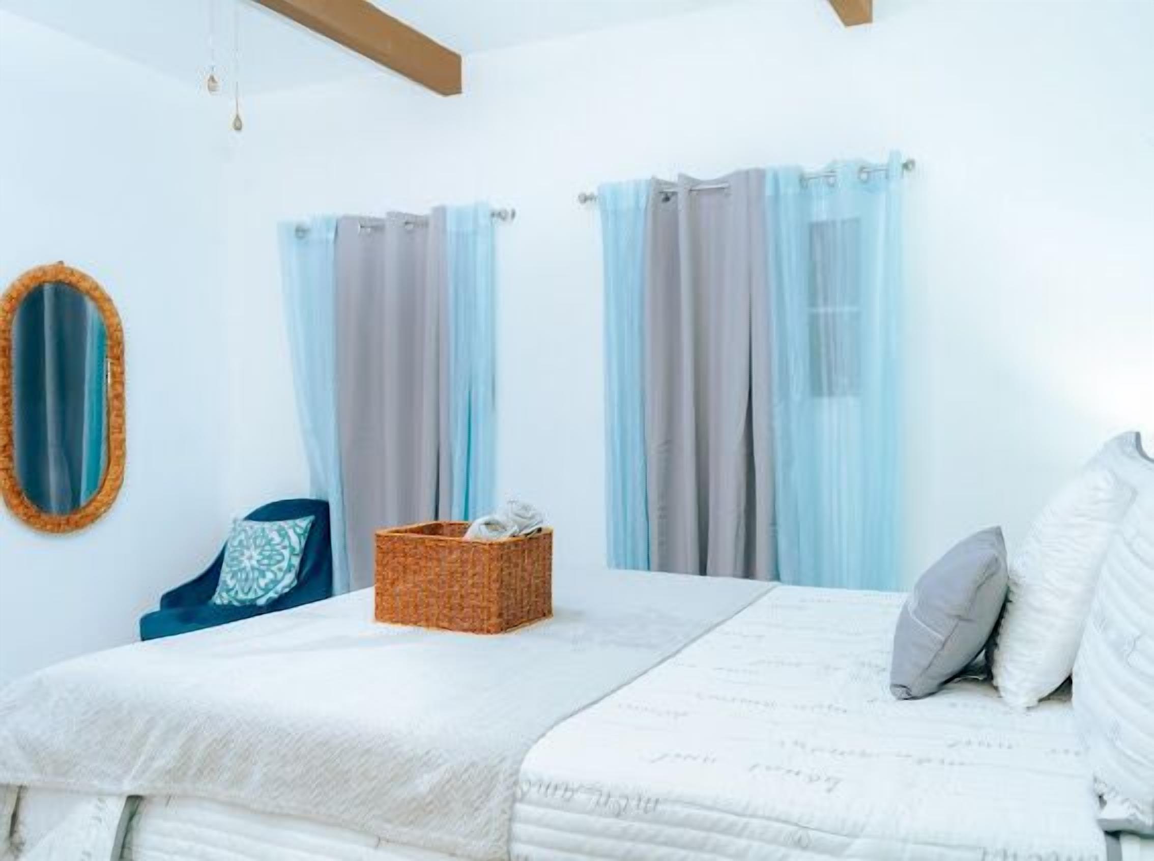 A bedroom with a bed, a blue chair, a wicker basket, and curtains.