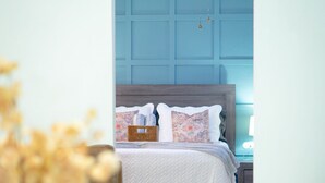 A bedroom with a bed, bedside tables, a clock, and a blue door.