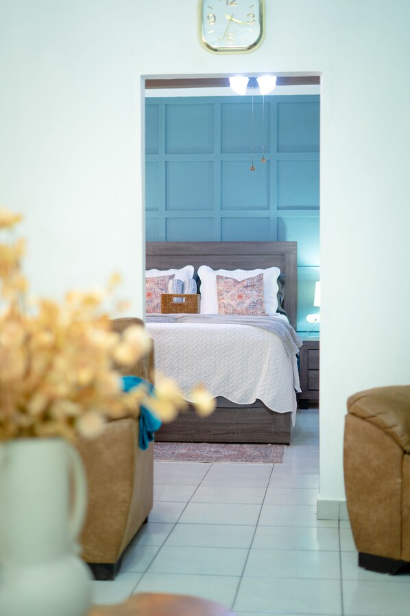 A bedroom with a bed, bedside tables, a clock, and a blue door. - Top Rated Home in Quezaltepeque, only 15 min away from San Salvador 🌅 (Quezaltepeque)