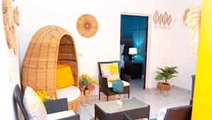 A cozy living area with wicker furniture, a glass coffee table, and a view into a bedroom.