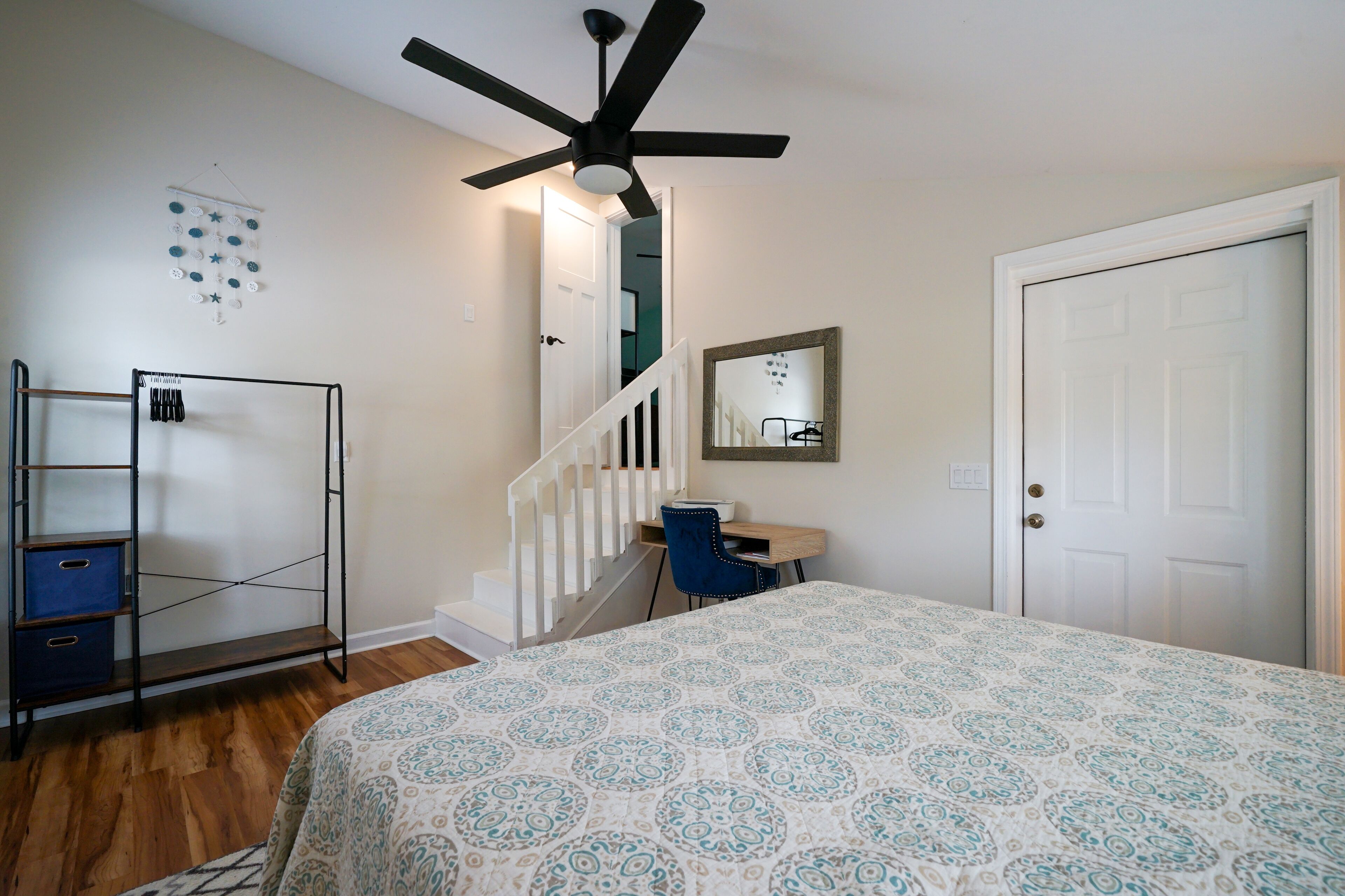 Une chambre à coucher comprenant un lit, un bureau, une chaise, une armoire, un ventilateur de plafond et un escalier.