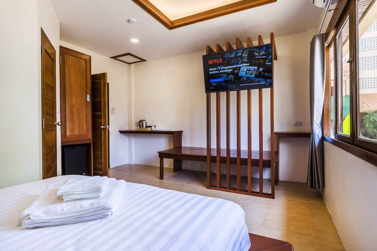 Quarto de hotel com uma cama, uma escrivaninha, uma televisão fixada em uma divisória de madeira e uma janela com vista.