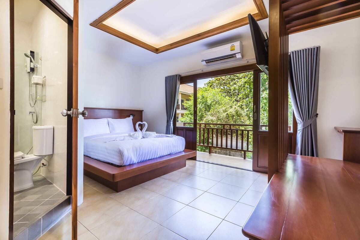 Quarto de hotel com cama, chuveiro e varanda com vista para vegetação.