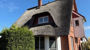 Uma casa com telhado de colmo, fachada de tijolo e janela com persianas.