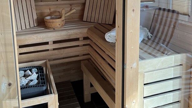 Uma sauna de madeira com bancos, um banco de madeira com uma cesta e uma pequena mesa de madeira.