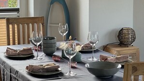 Mesa de jantar posta com pratos, tigelas e taças de vinho, um vaso decorativo e uma escultura azul singular.