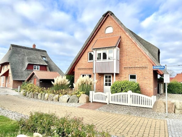 A traditional brick house with a steeply pitched roof, a small balcony, and a gravel driveway.