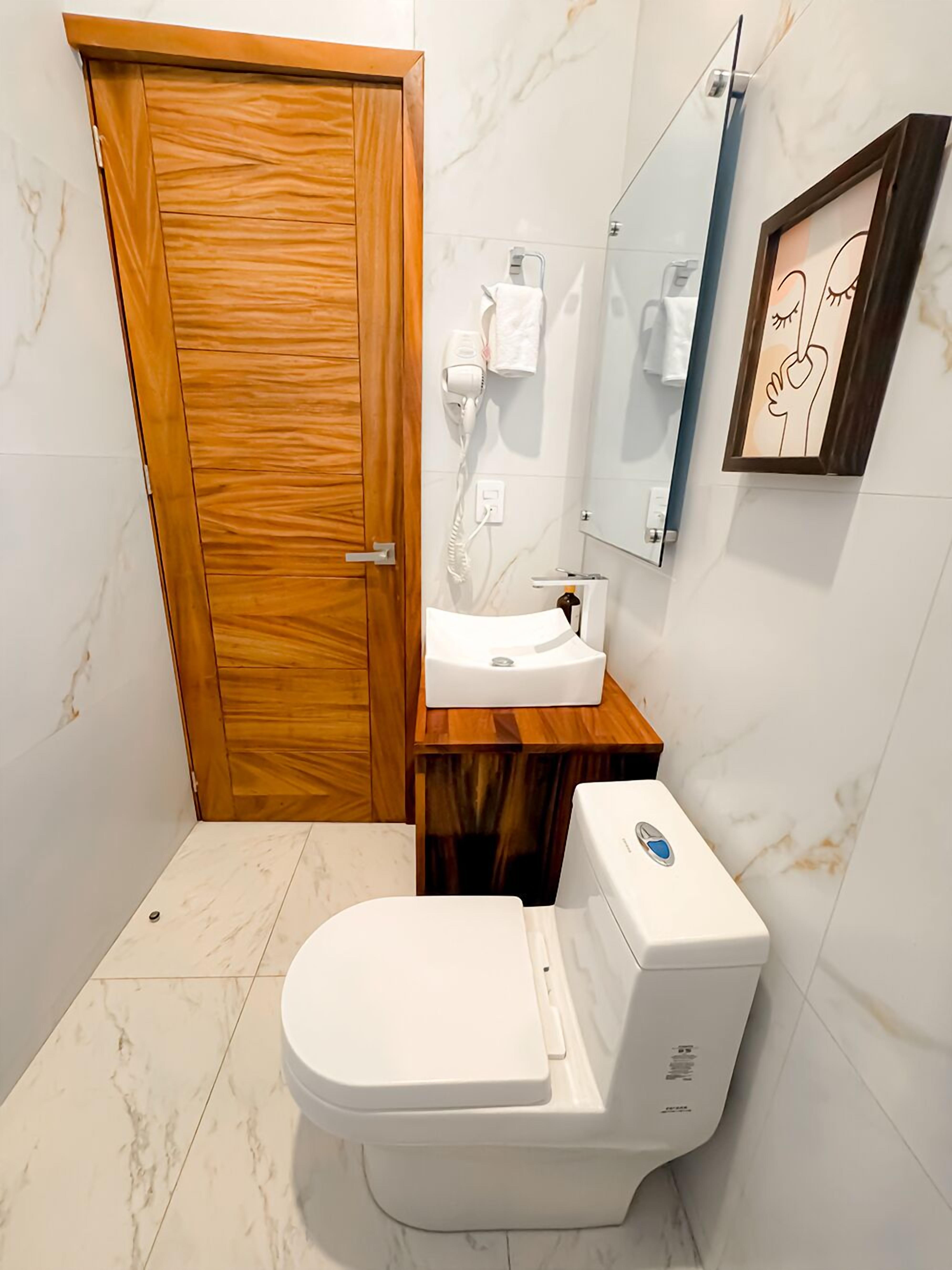 Un baño con puerta de madera, inodoro blanco, lavamanos y espejo.