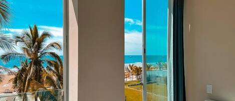 A room with a large window overlooking a beach, palm trees, and a clear blue sky.