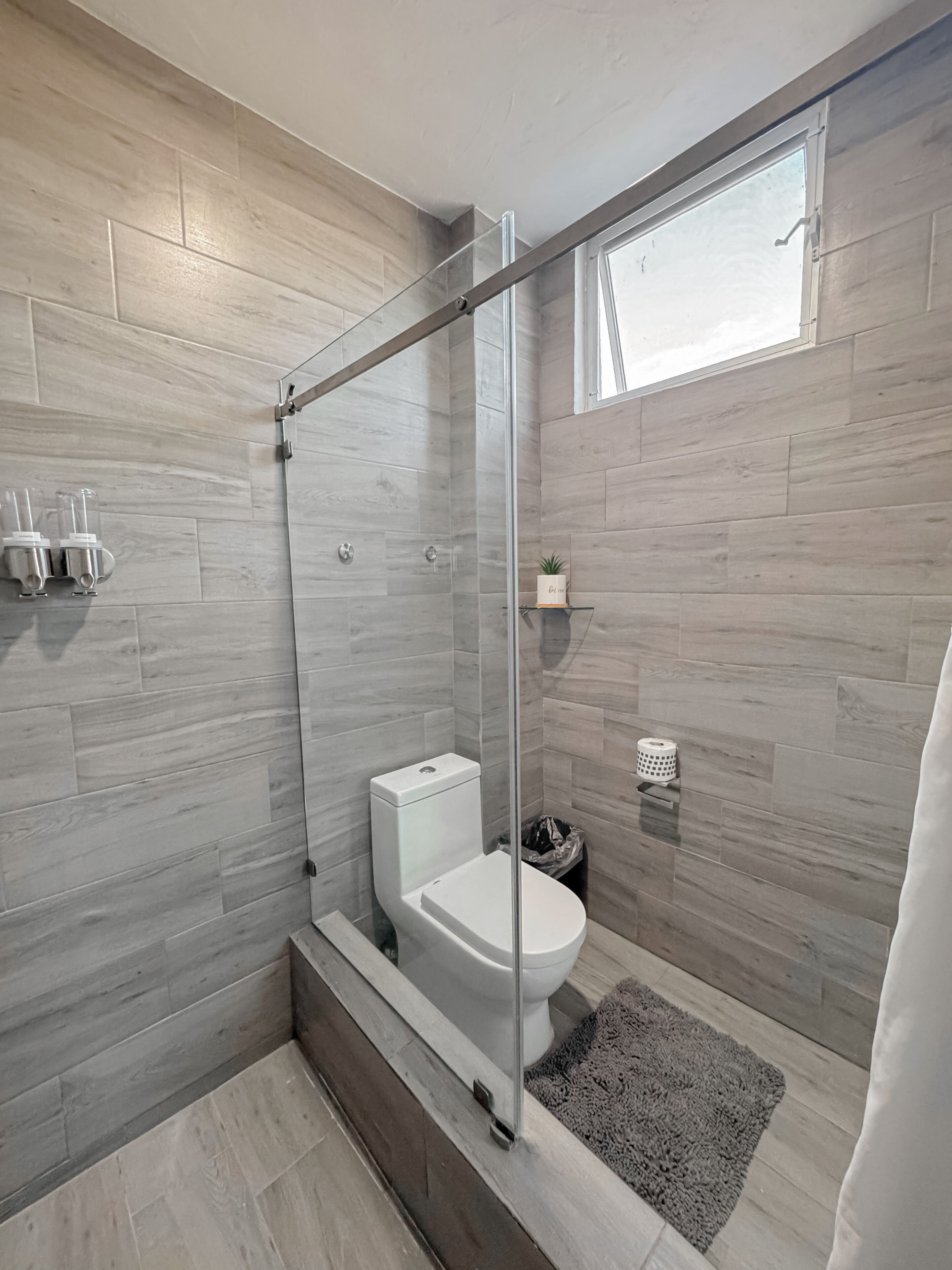 Un baño moderno con ducha envuelta en vidrio, inodoro y un estante pequeño con artículos de tocador.