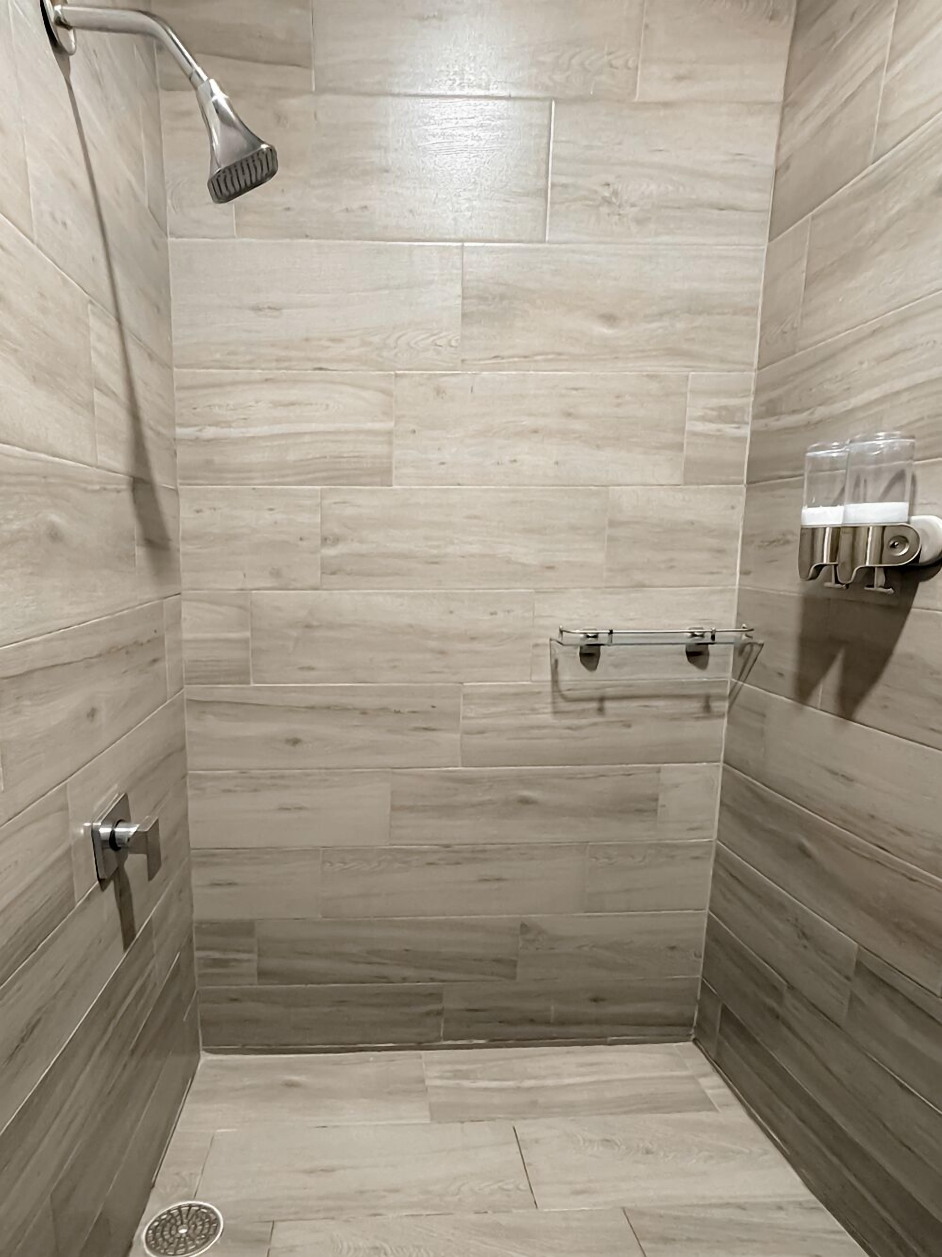 Una dutxa amb un braç de dutxa portàtil, un suport per a tovalloles i un dosificador de sabó.