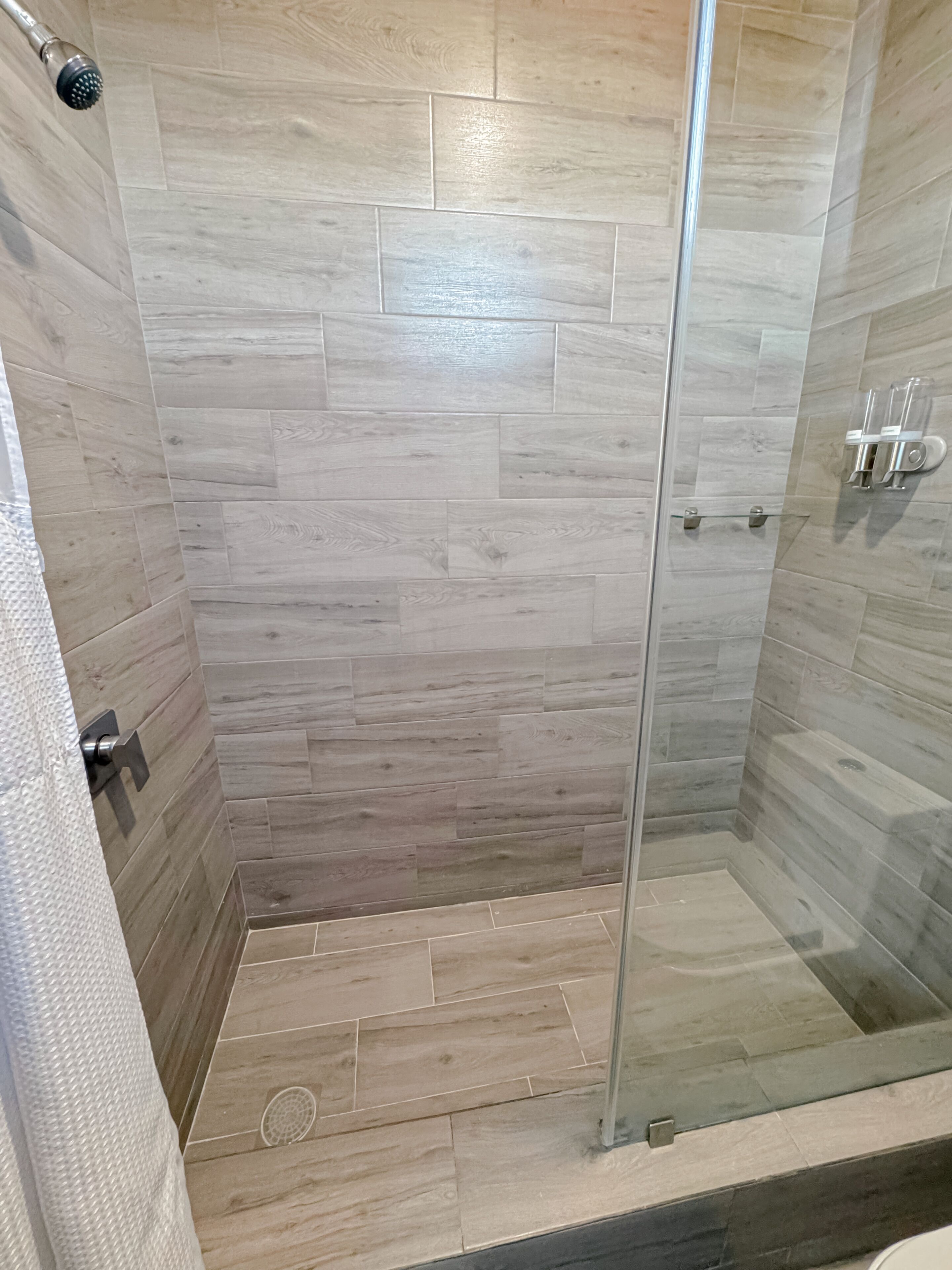 Een douche met glazen deur, betegelde wanden en een houten vloer.