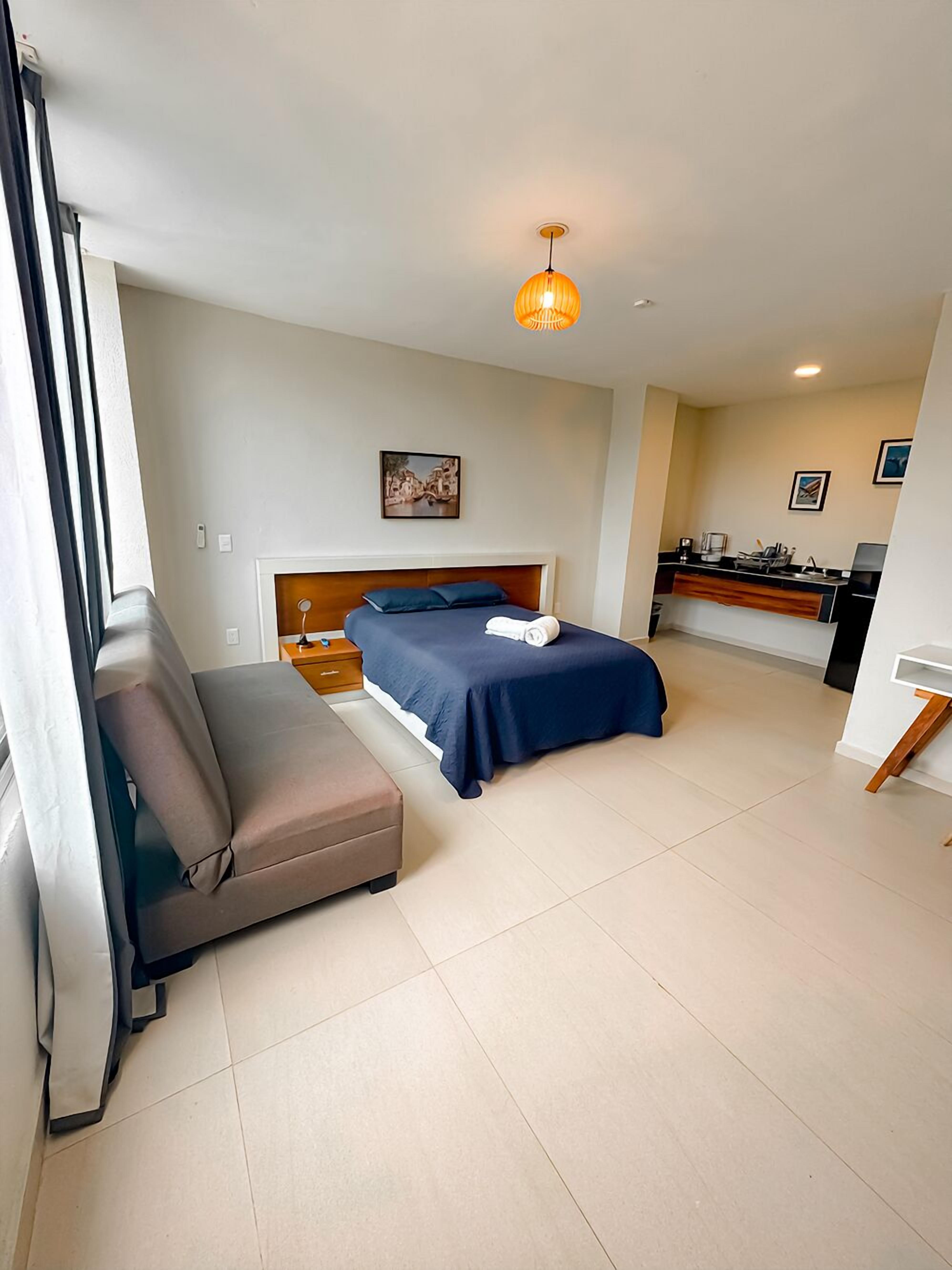 Una habitación de hotel moderna con cama, sofá, una pequeña cocina y una mesa de comedor.