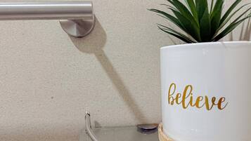 A white mug with the word "believe" in gold lettering, placed on a glass table with a woven coaster.