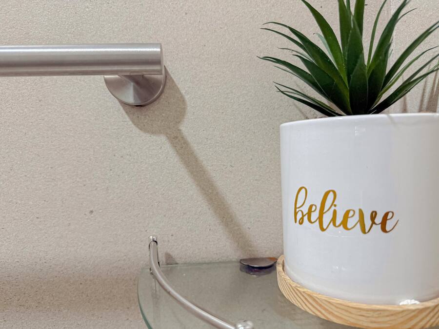 A white mug with the word "believe" in gold lettering, placed on a glass table with a woven coaster.