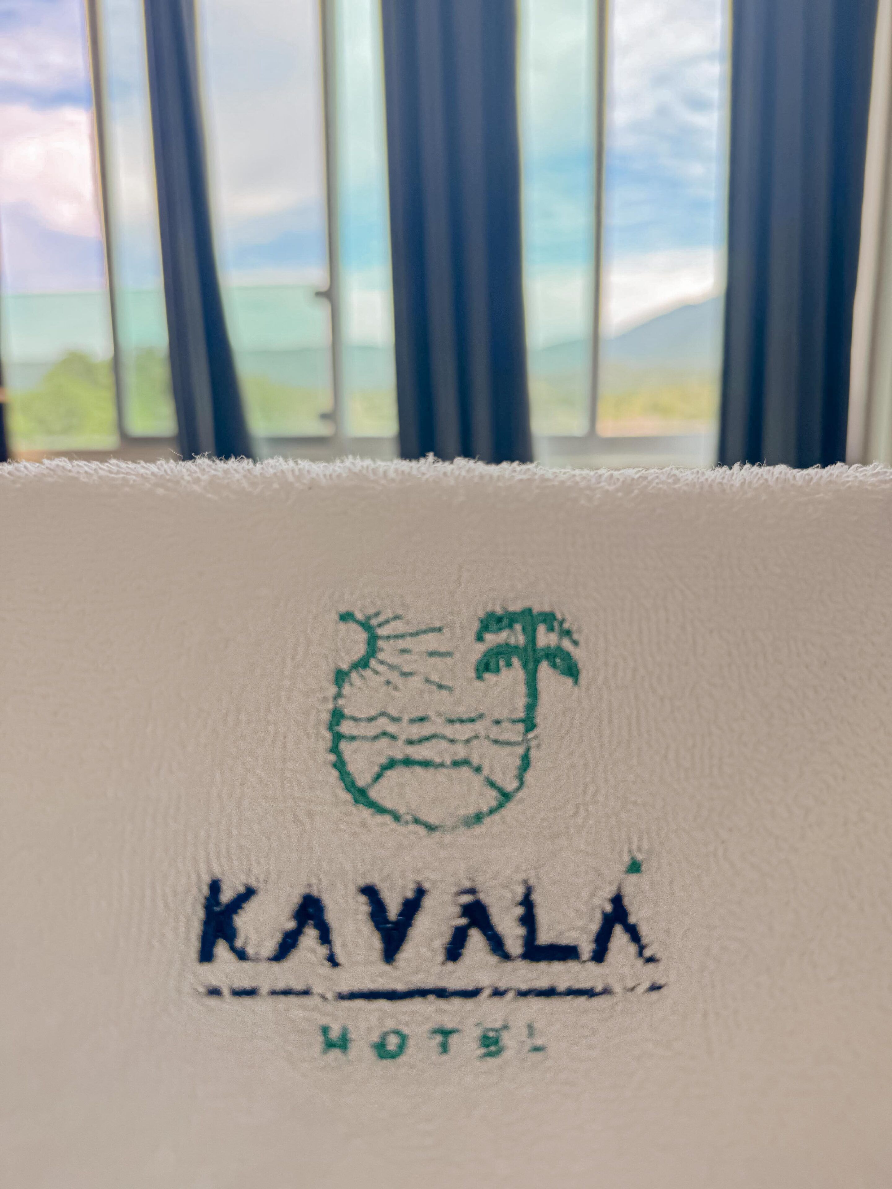 A white pillow with the Kavala Hotel logo and name embroidered on it.