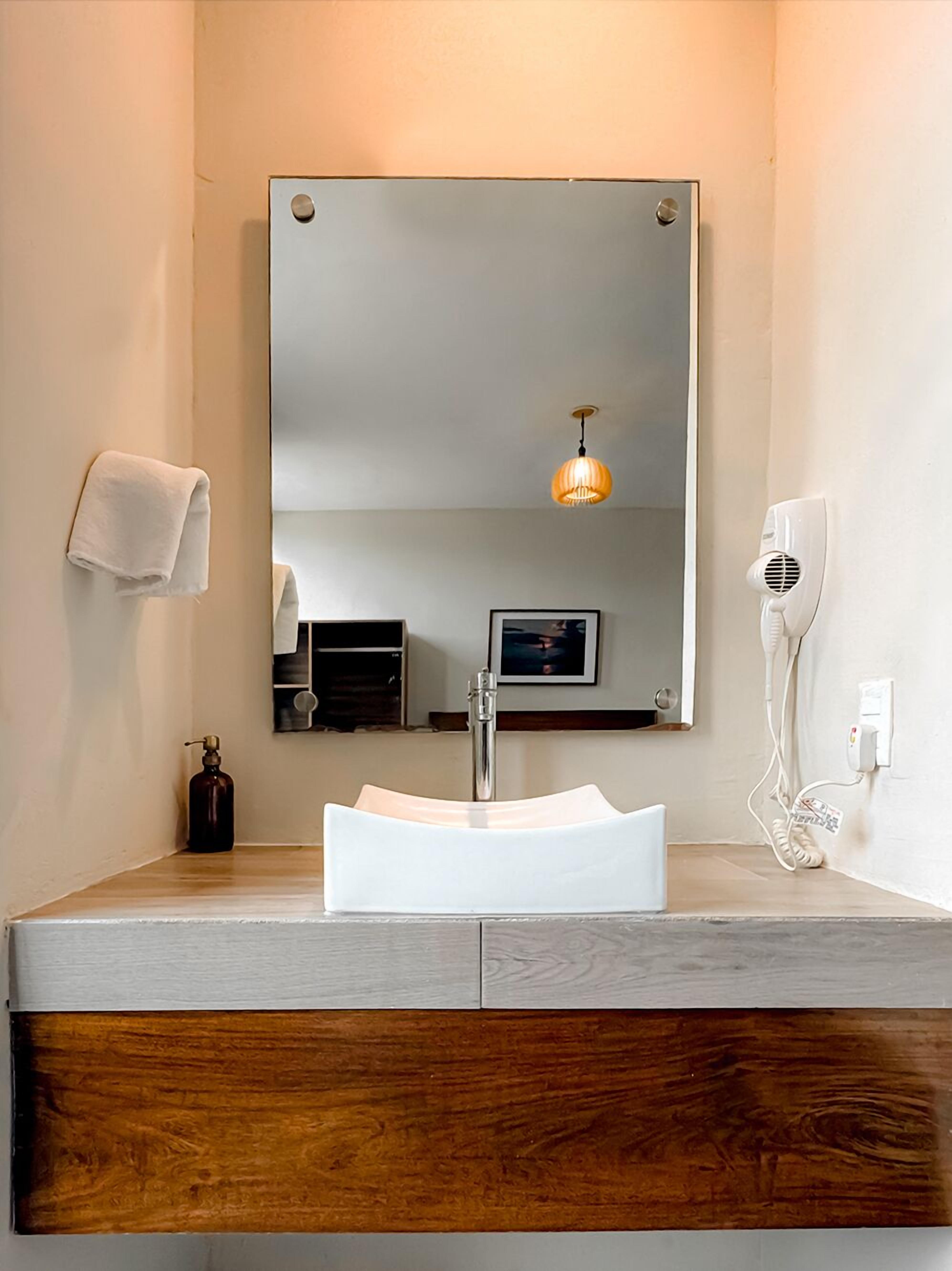 Une salle de bain avec un lavabo blanc, un miroir, un porte-serviettes, un sèche-cheveux et un distributeur de savon.