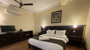 Une chambre d’hôtel avec un grand lit, un bureau avec une télévision, une machine à café et un ventilateur de plafond.