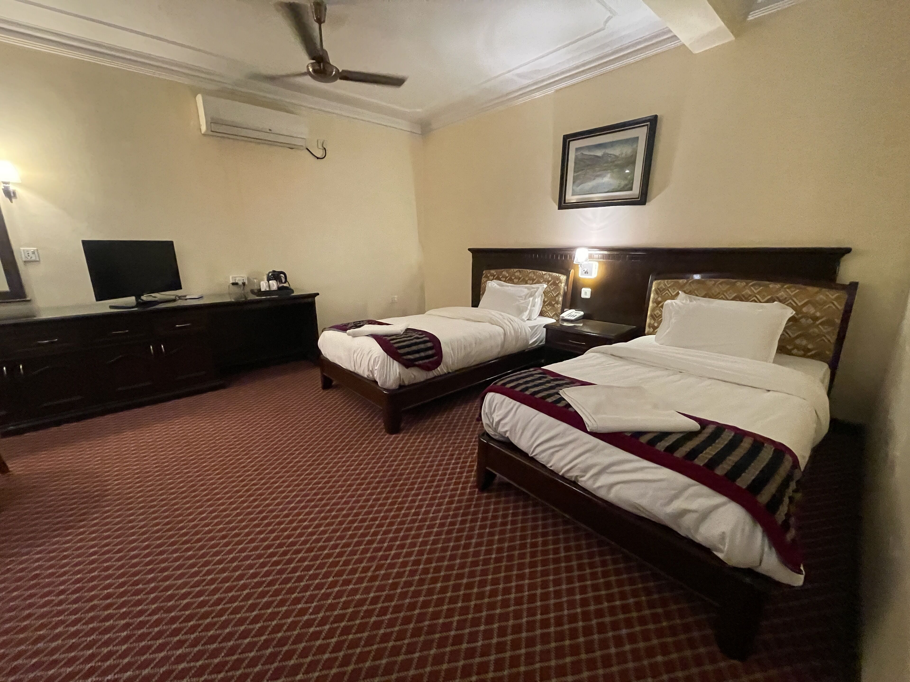 Een hotelkamer met twee bedden, een bureau, een flatscreen televisie, een koffiezetapparaat en een lijst aan de muur.