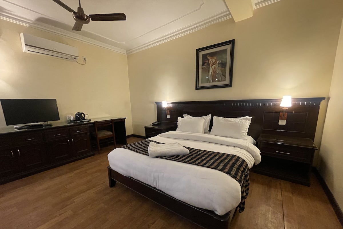 Habitación de hotel con cama, mesitas de noche, escritorio con silla, televisor y aire acondicionado.