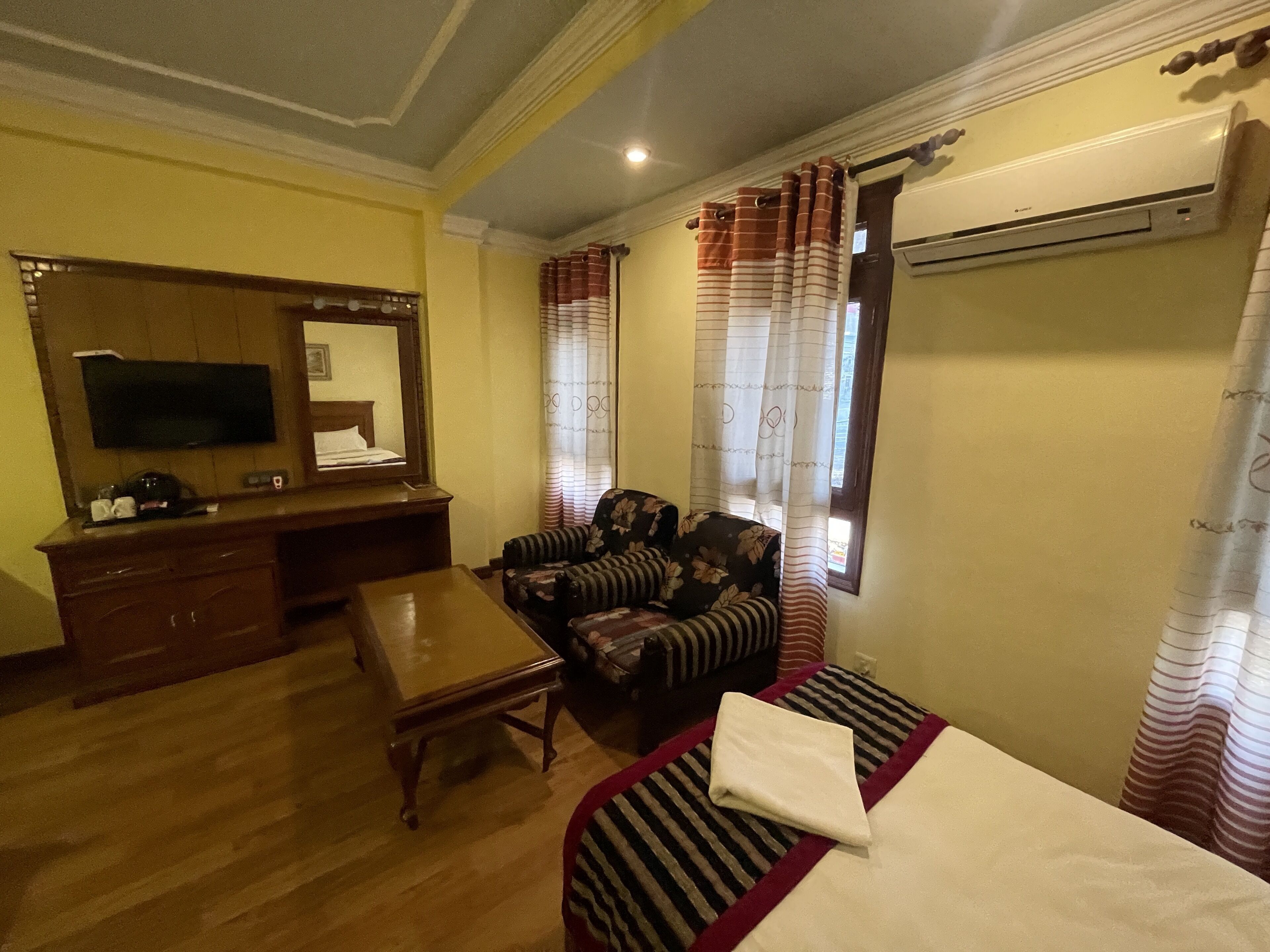 A hotel room with a wooden desk, a television, a sofa, and a bed with striped bedding.