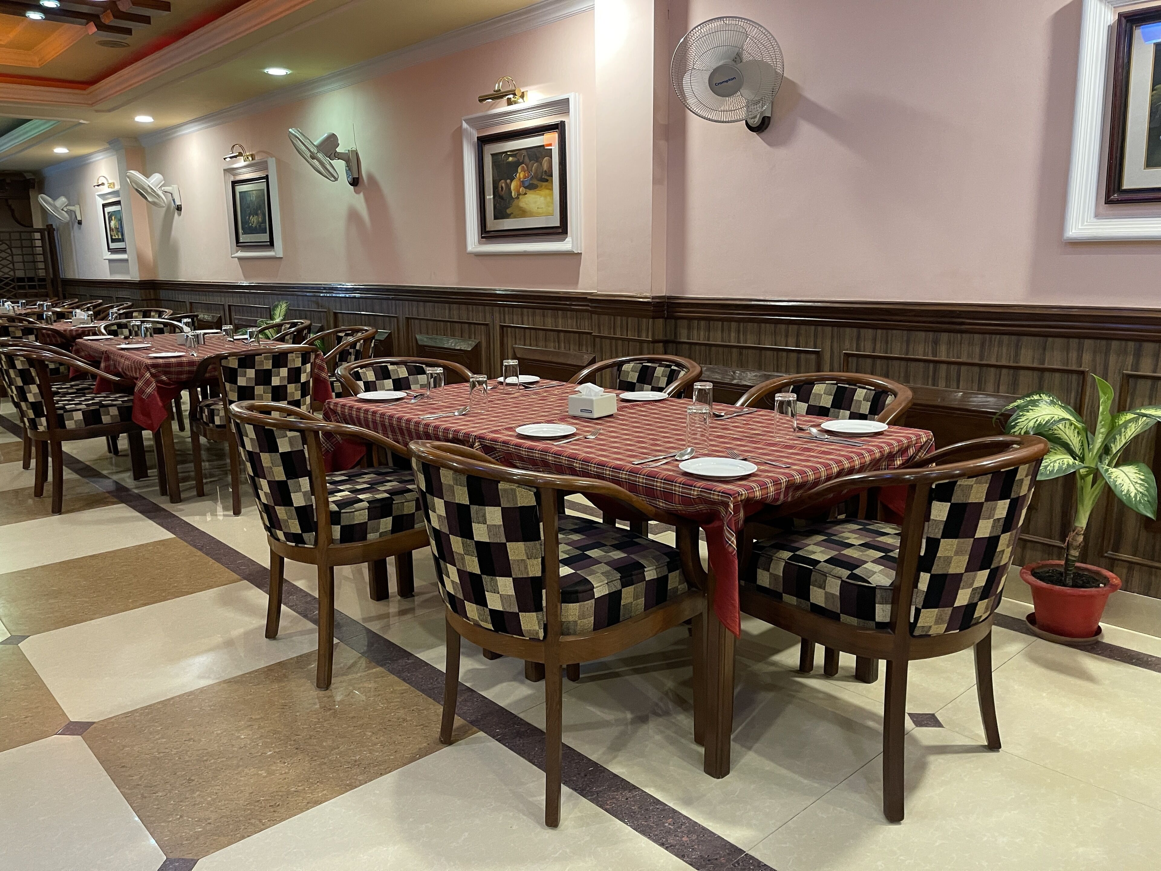 A restaurant with checkered tablecloths, wooden chairs, and framed artwork on the walls.