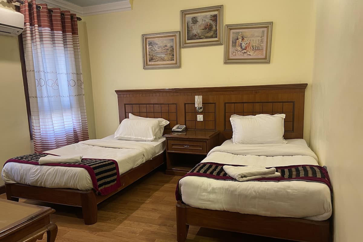Una habitación de hotel con dos camas individuales, una mesita de noche de madera, un teléfono y una pequeña mesa.
