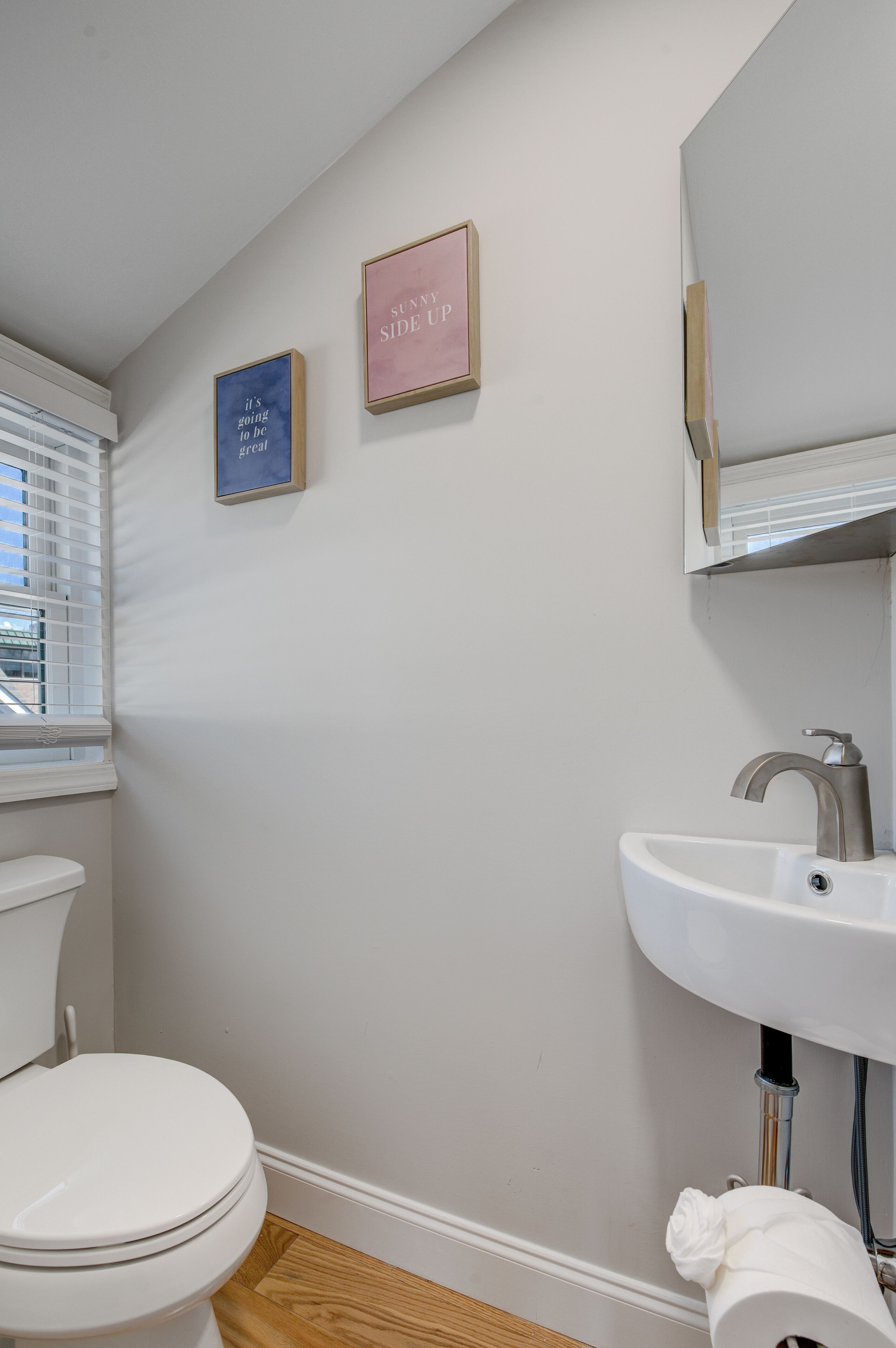 A bathroom with a toilet, sink, and two framed motivational quotes on the wall.