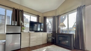 A modern living room with a flat-screen TV, a fireplace, and a large window with curtains. - Silicon Valley Hideaway w/ Private Garden (San Jose)