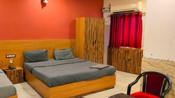 A bedroom with a wooden bed, a wardrobe, a chair, and a small bedside table. - Nirmalya plaza (Brahmapur)