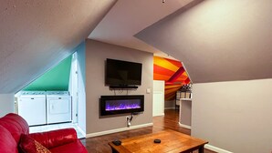 Un salon avec un canapé rouge, une table basse en bois, un téléviseur à écran plat et une cheminée.
