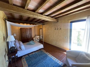 Ein Schlafzimmer mit Baldachinbett, einem Holzschrank, einem Stuhl und Blick ins Freie.