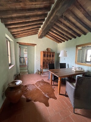 Ein rustikales Zimmer mit Holzbalkendecke, einem Esstisch, Stühlen, einem Schrank und einem Kuhfellteppich.