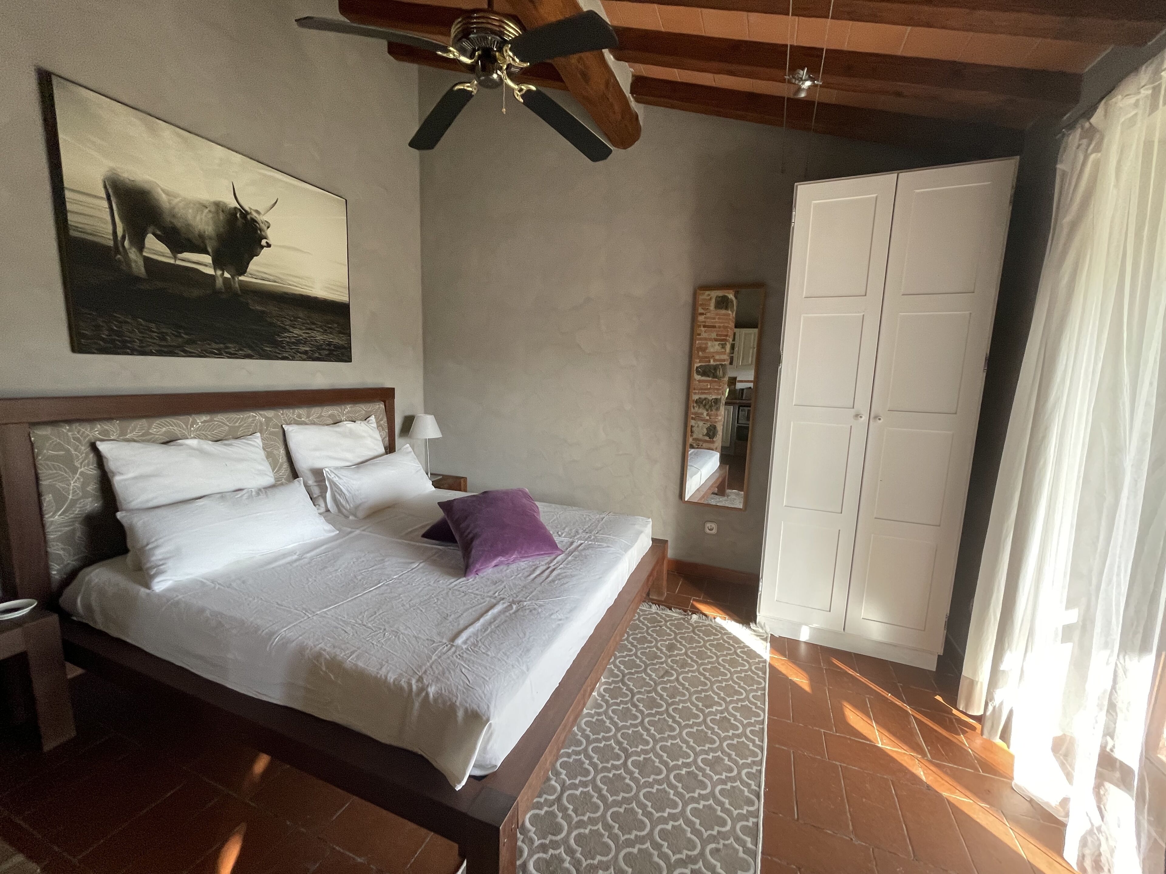 Een slaapkamer met een bed, een plafondventilator, een schilderij, een kledingkast en een kamerkleed met een patroon.
