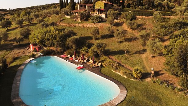 A large, curved swimming pool surrounded by a wooden deck with lounge chairs and umbrellas. - Charming Cottage overlooking the pool and the beautiful Tuscan landscape  (Toscana)