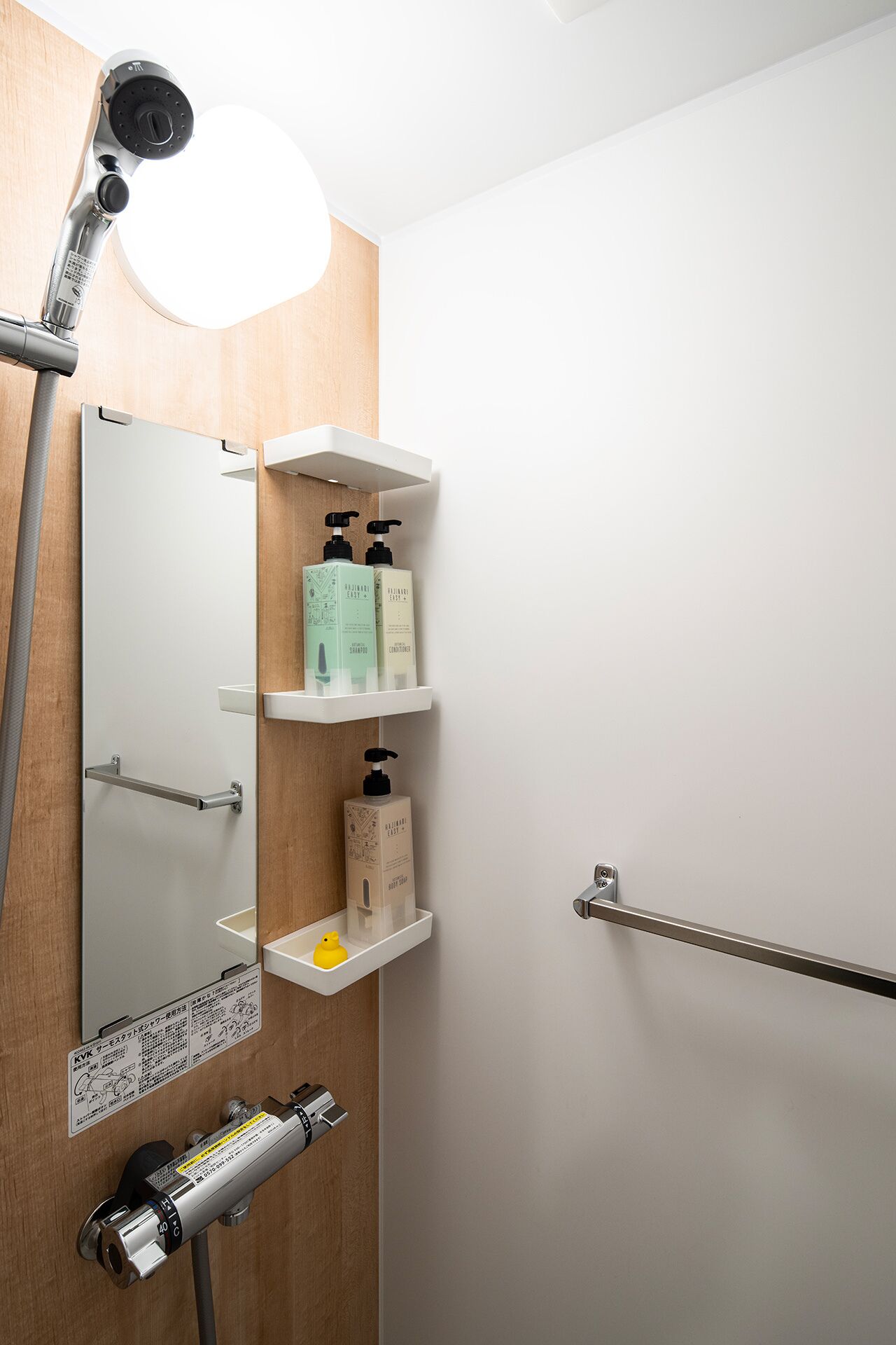 Ein Badezimmer mit Spiegel, Ablagen für Toilettenartikel, einer Handtuchstange und einer Handbrause.