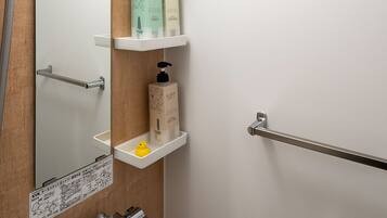 A bathroom with a mirror, shelves with toiletries, a towel bar, and a handheld showerhead.