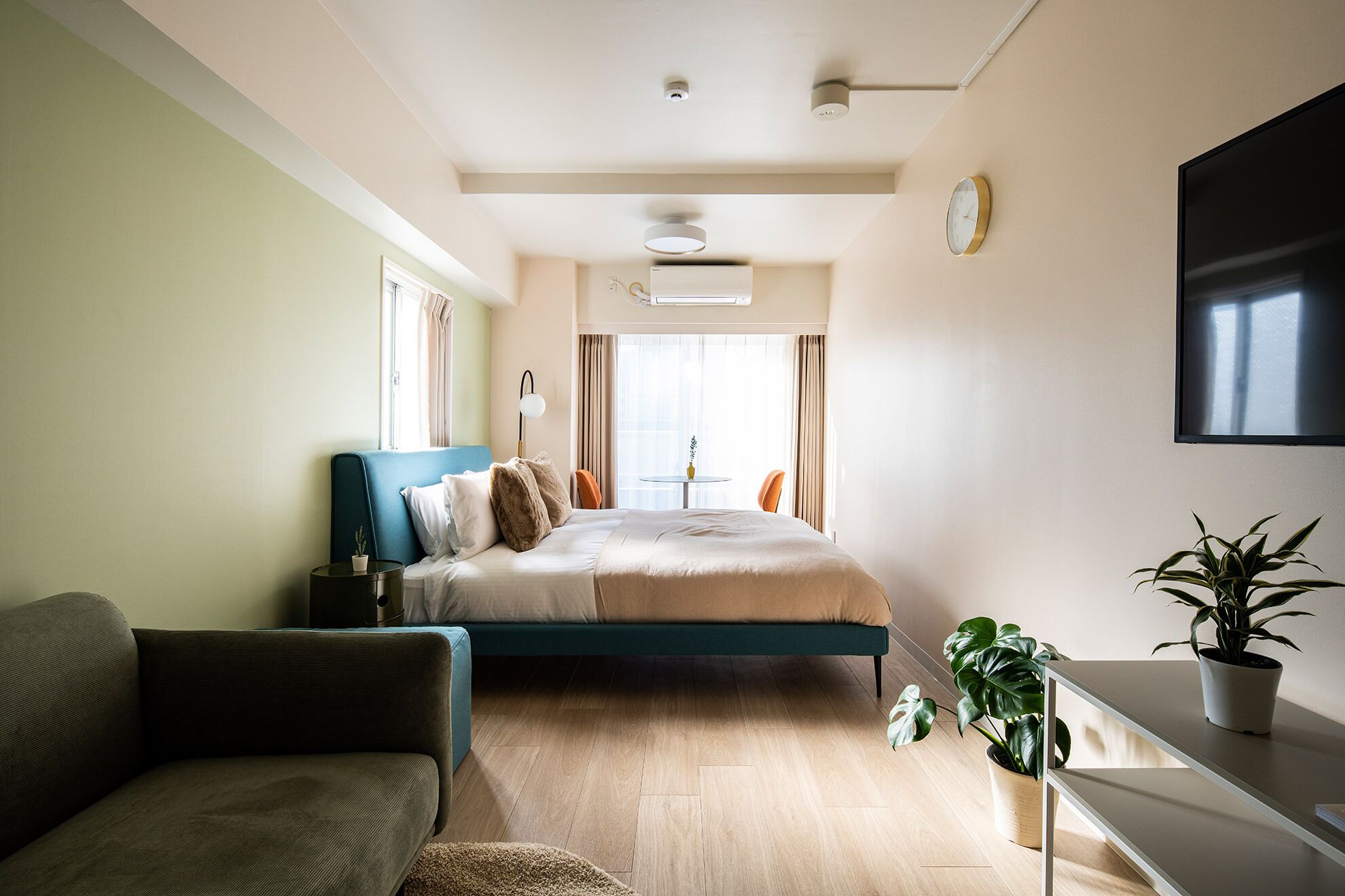 A modern hotel room with a bed, a sofa, a desk, and a potted plant.