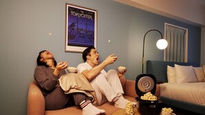 Un salon avec un canapé, une table basse sur laquelle se trouve un bol de pop-corn, une affiche accrochée au mur et une lampe.