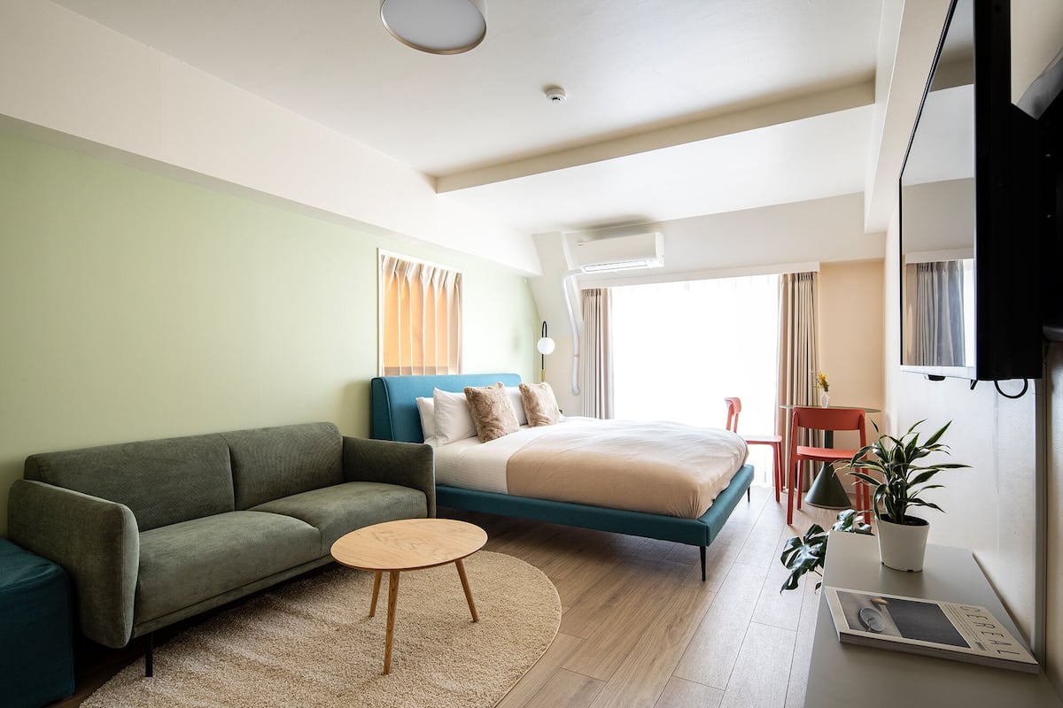 A modern hotel room with a bed, a sofa, a small round table, and a TV.