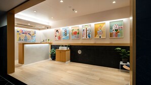 Un espace d’accueil moderne avec un comptoir de réception en bois, un mur noir orné d’une grille circulaire et une série d’œuvres d’art colorées accrochées au mur.