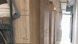 A corridor with wooden wardrobes labeled with numbers, a bunk bed with grey bedding, and a bright hallway. - Gents House - Hostel (Taipei)