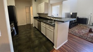 A modern kitchen with dark tiled flooring, white cabinetry, a black countertop, and a built-in dishwasher.