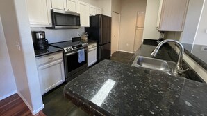 A kitchen with white cabinets, a black stove, a microwave, a refrigerator, and a sink.