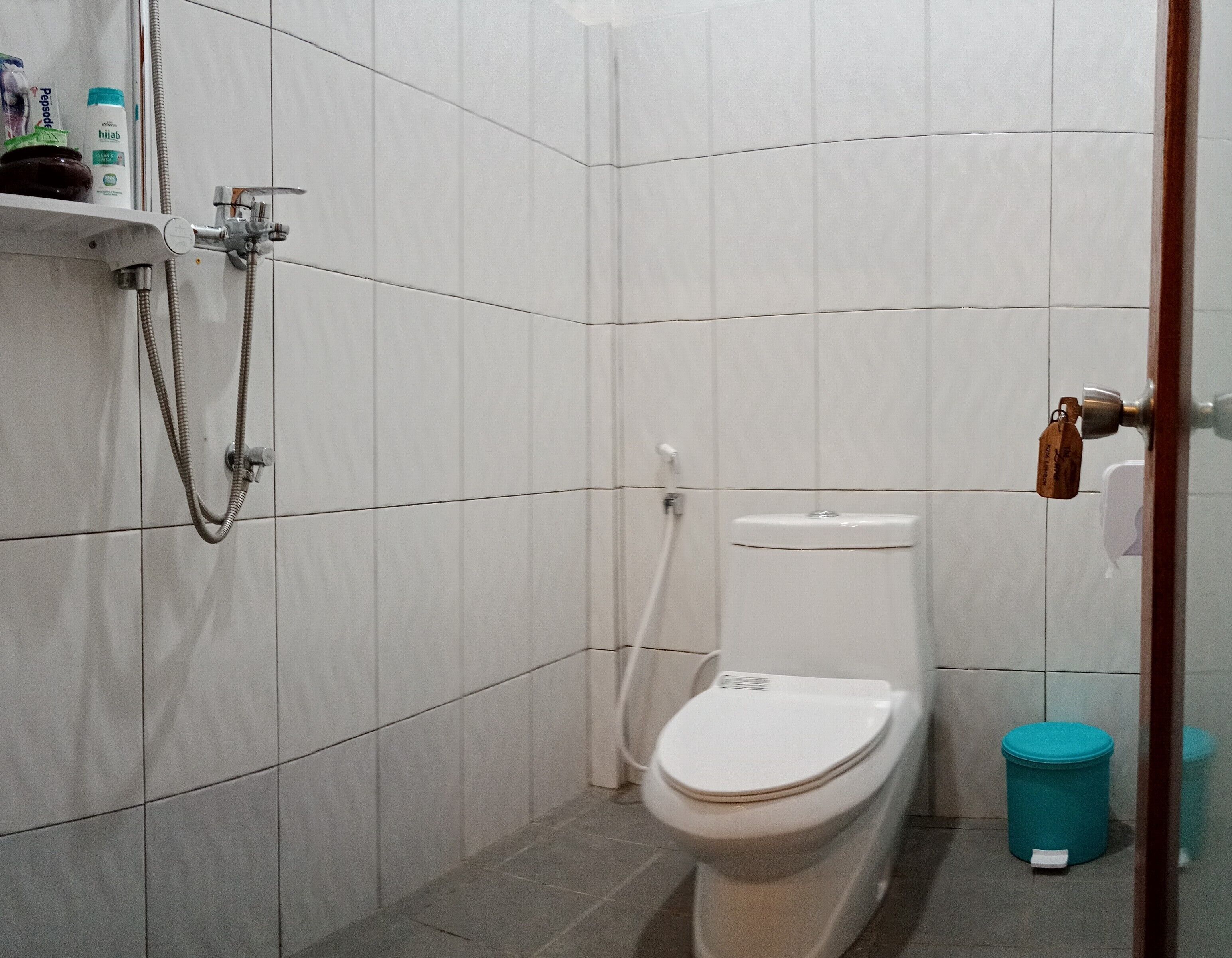 Un bagno piccolo e moderno rivestito di piastrelle bianche, con un water, una doccetta e un cestino.
