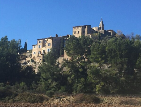 Un bâtiment historique en pierre, à plusieurs étages, entouré d’une végétation dense et surplombé d’un ciel bleu clair.
